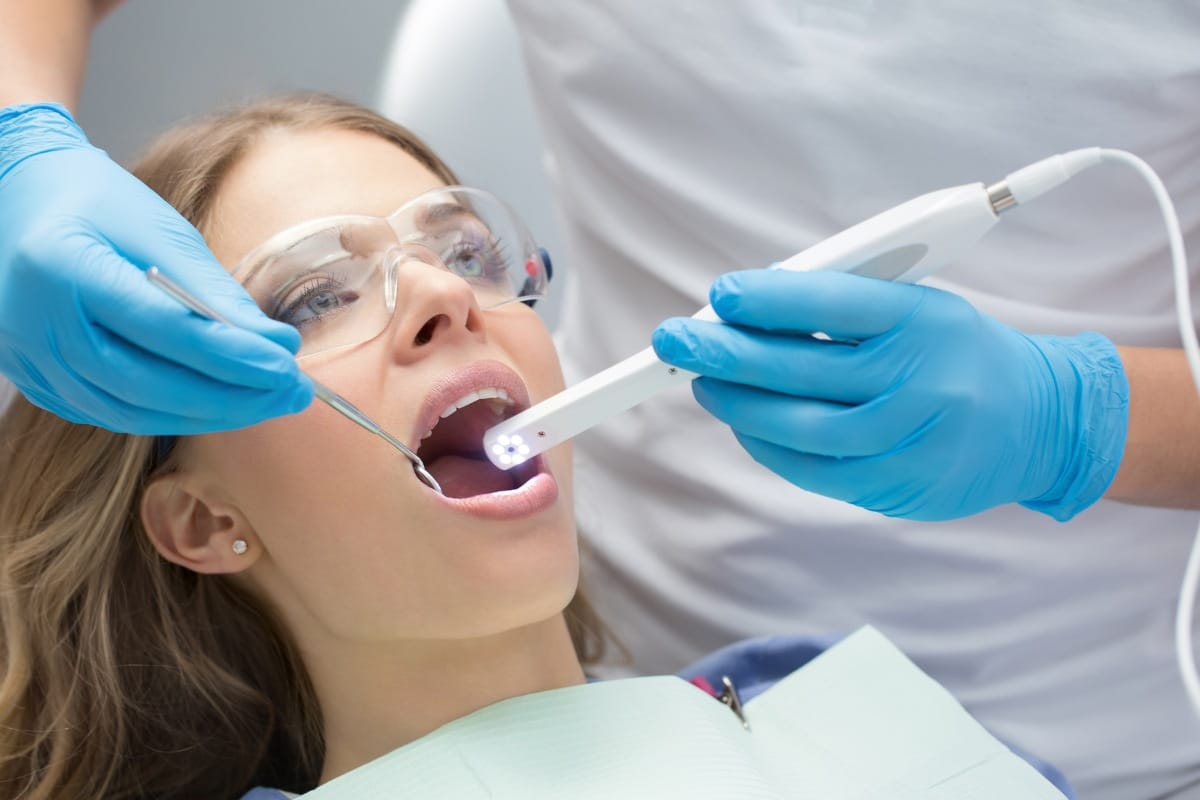 Dentist using an intraoral camera to examine a patient’s teeth while she wears protective eyewear during a dental checkup.
