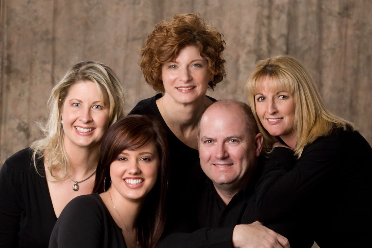 Group pof people of all ages in black shits smiling in front of a beige backdrop