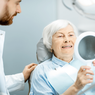 Older woman looking in a mirror at her new teeth, representing dental implants in chesapeake va