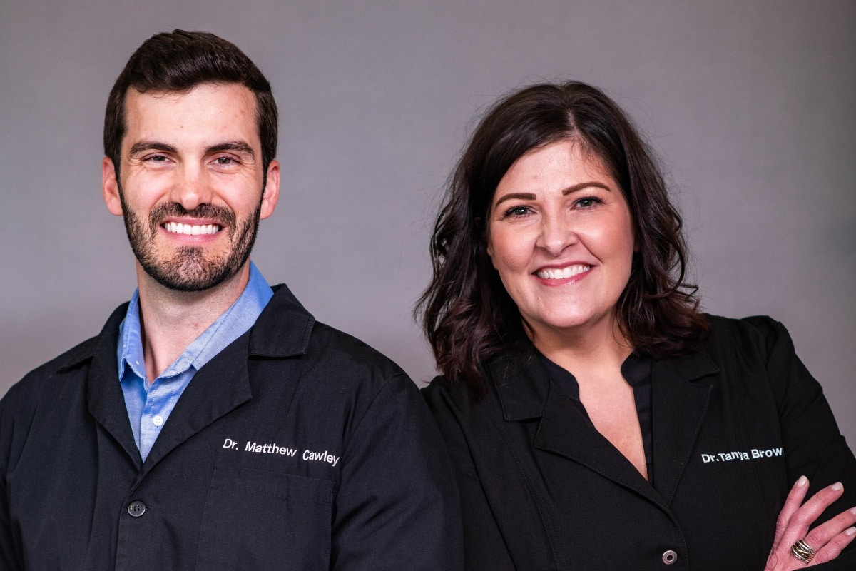 Expert cosmetic dentists dr. Matthew cawley and dr. Tanya brown smiling in black coats at their chesapeake dental practice.