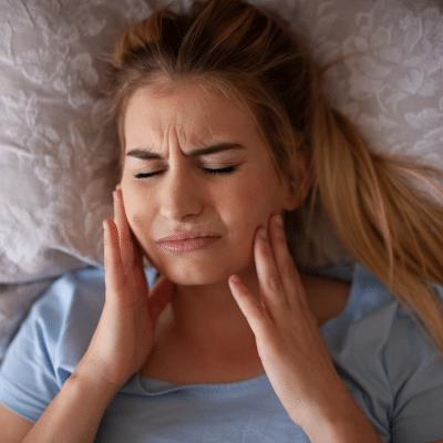 Woman experiencing jaw pain in bed, representing tmj jaw pain and sleep